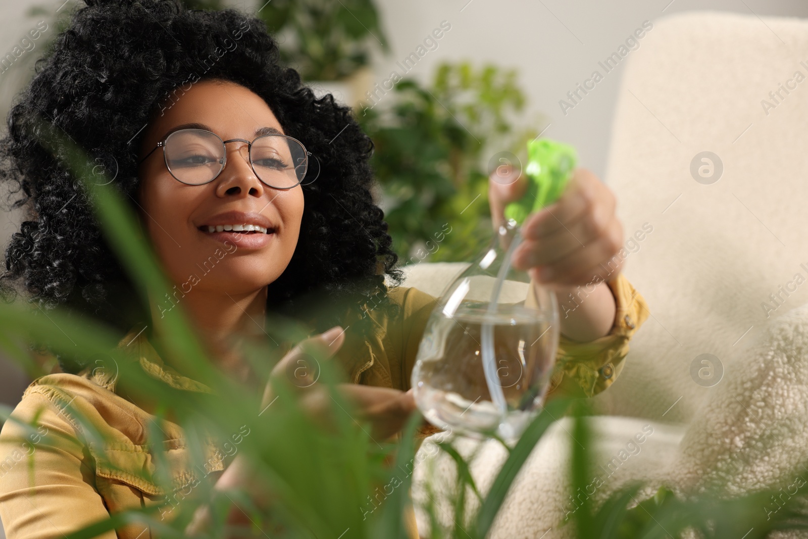 Photo of Happy woman spraying beautiful houseplant leaves with water indoors