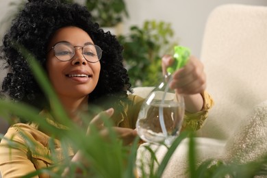 Happy woman spraying beautiful houseplant leaves with water indoors