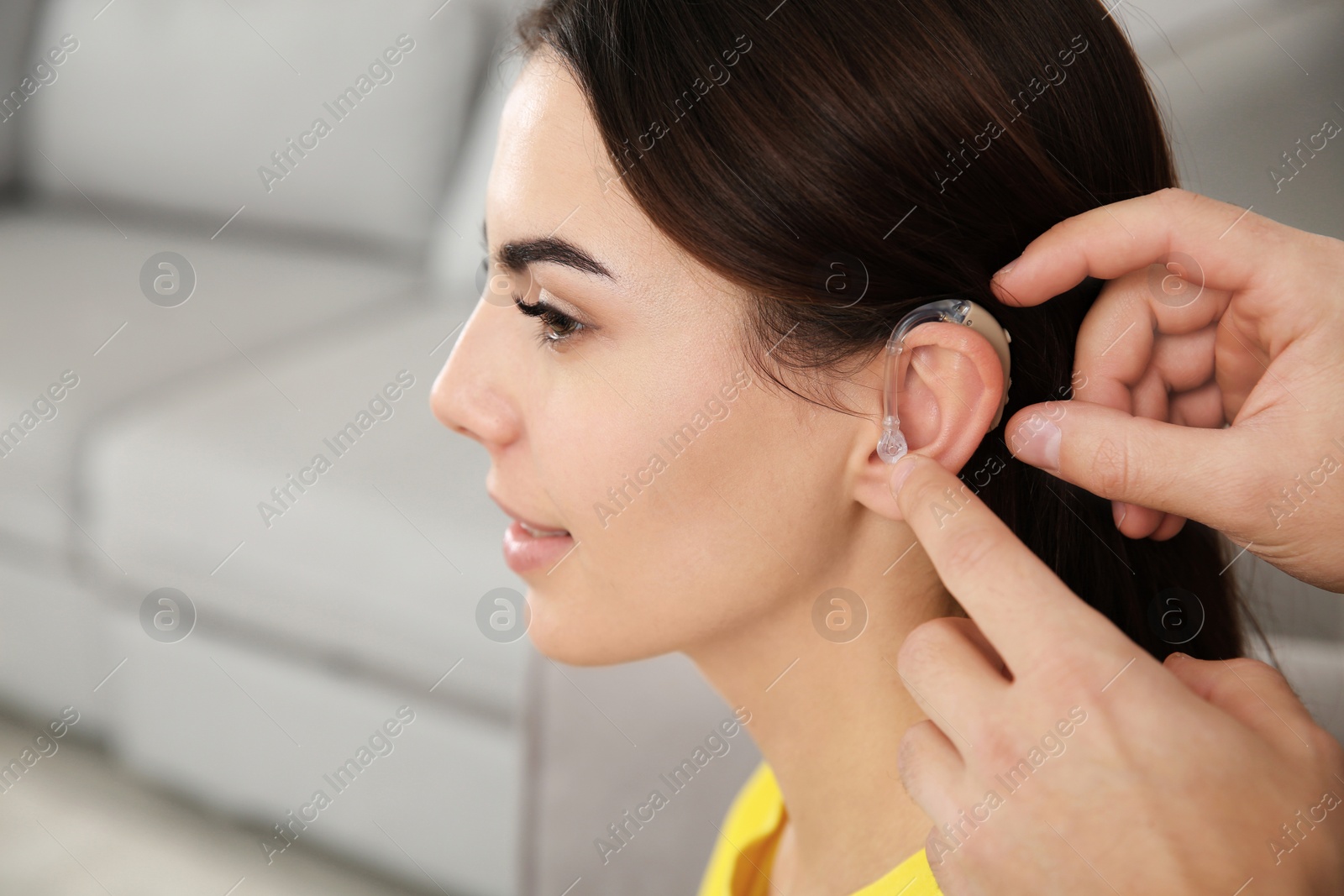 Photo of Man putting hearing aid in woman's ear indoors, closeup