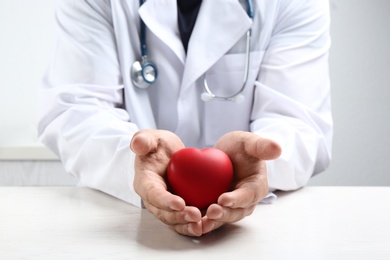 Photo of Doctor with red heart at white table indoors, closeup