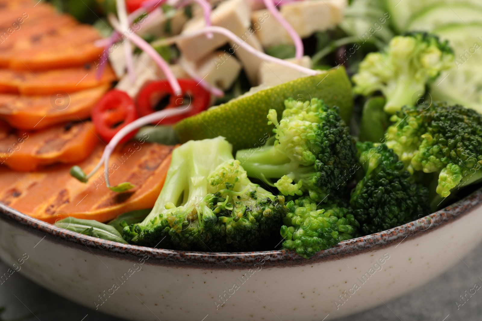Photo of Bowl with many different vegetables on grey table, closeup. Vegan diet