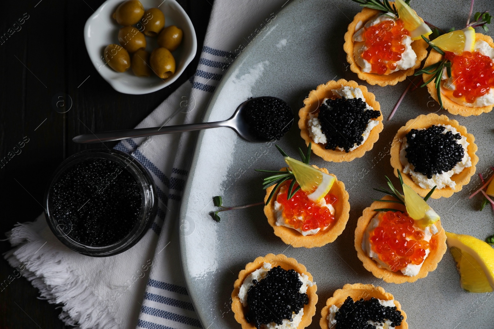 Photo of Delicious tartlets with red and black caviar served on dark table, flat lay