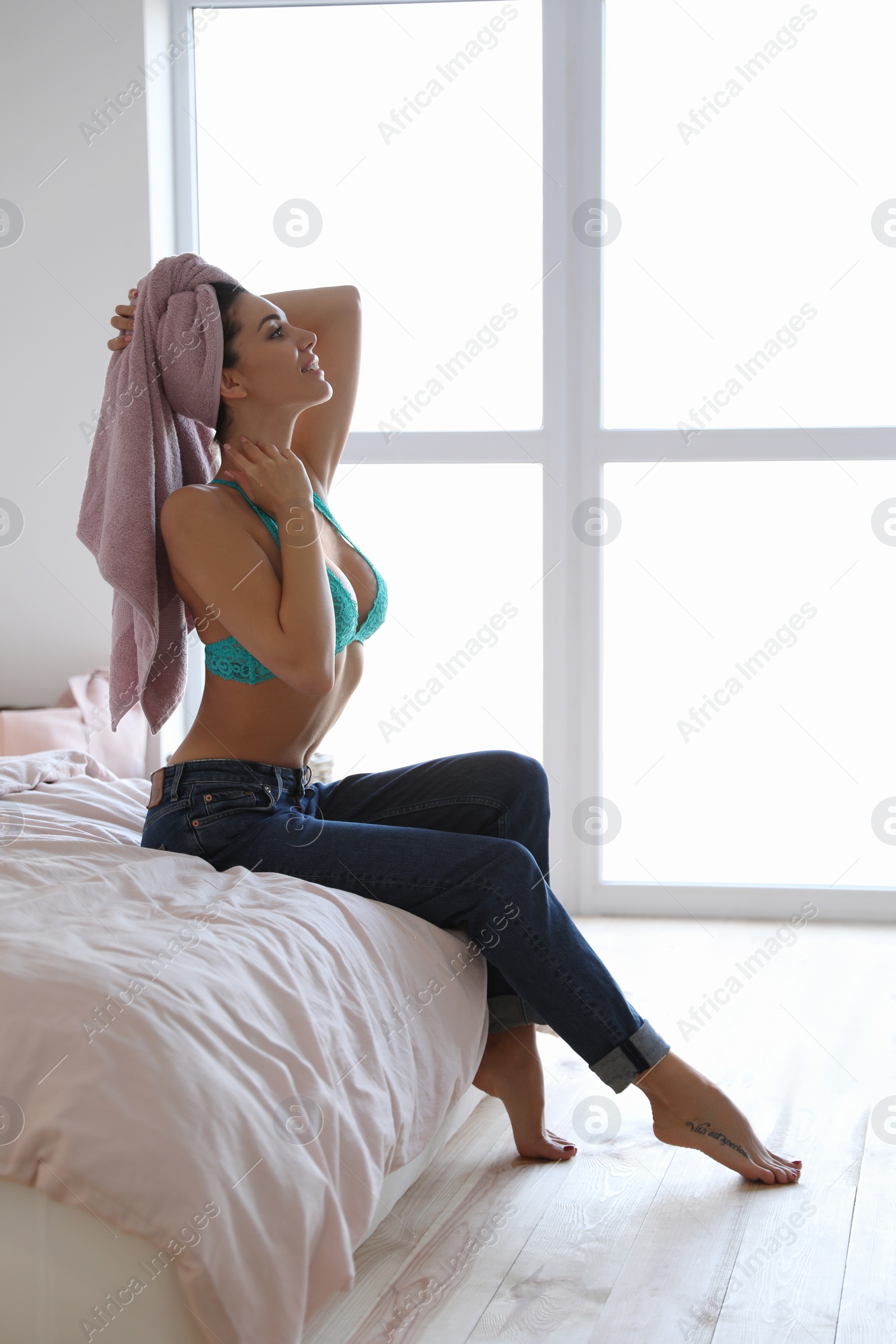 Photo of Pretty young woman with towel on her head sitting on bed at home