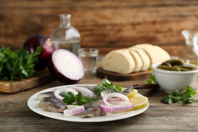 Photo of Sliced salted herring fillet served with onion rings, parsley and lemon on wooden table