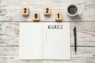 Photo of Notebook with word Goals near number 2021 made of cubes, new year aims. Objects on white wooden table, flat lay