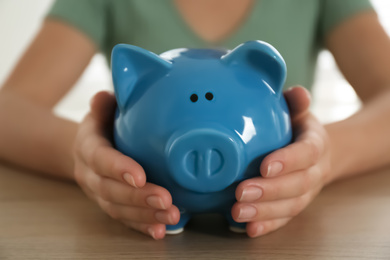 Photo of Woman with piggy bank at wooden table indoors, closeup