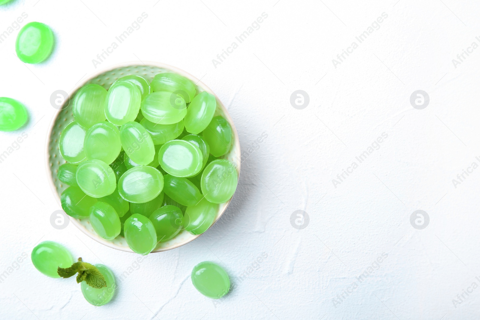 Photo of Bowl with tasty mint candies and leaves on light background, top view