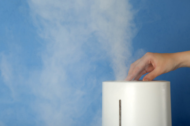 Photo of Woman using modern air humidifier on light blue background, closeup. Space for text