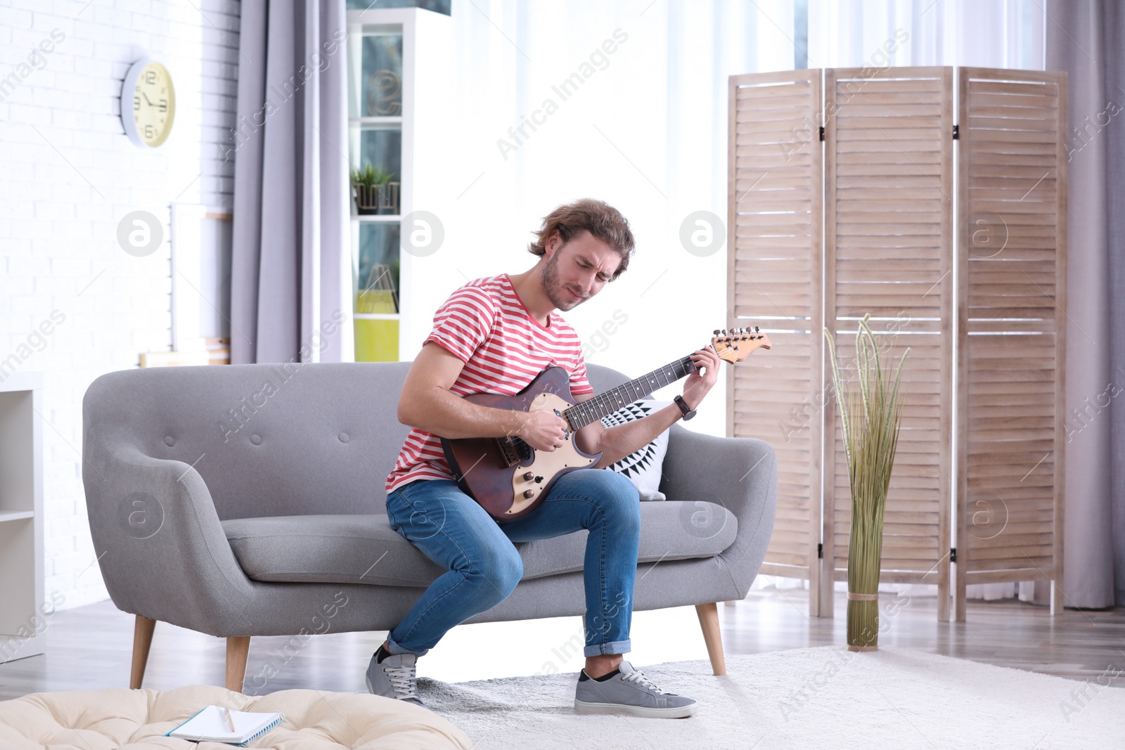 Photo of Young man playing electric guitar in living room