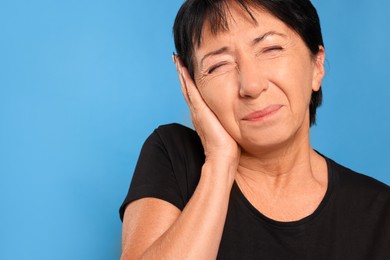 Senior woman suffering from ear pain on light blue background. Space for text