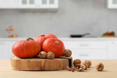 Photo of Fresh pumpkins and walnuts on wooden table in kitchen, space for text