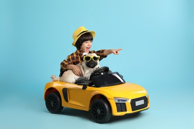 Little boy with his dog in toy car on light blue background