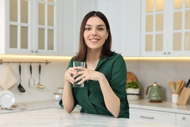Photo of Young woman holding glass with clean water in kitchen