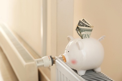 Photo of Piggy bank with money on heating radiator indoors