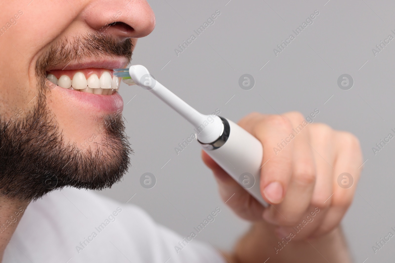 Photo of Man brushing his teeth with electric toothbrush on light grey background, closeup