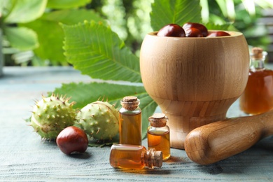 Mortar with pestle, chestnuts and bottles of essential oil on table against blurred background