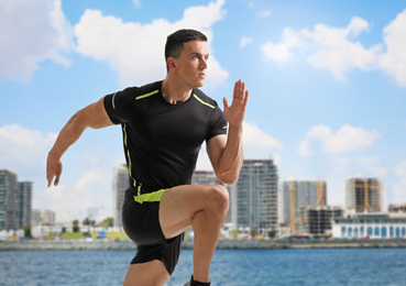 Image of Athletic young man running near sea on sunny day