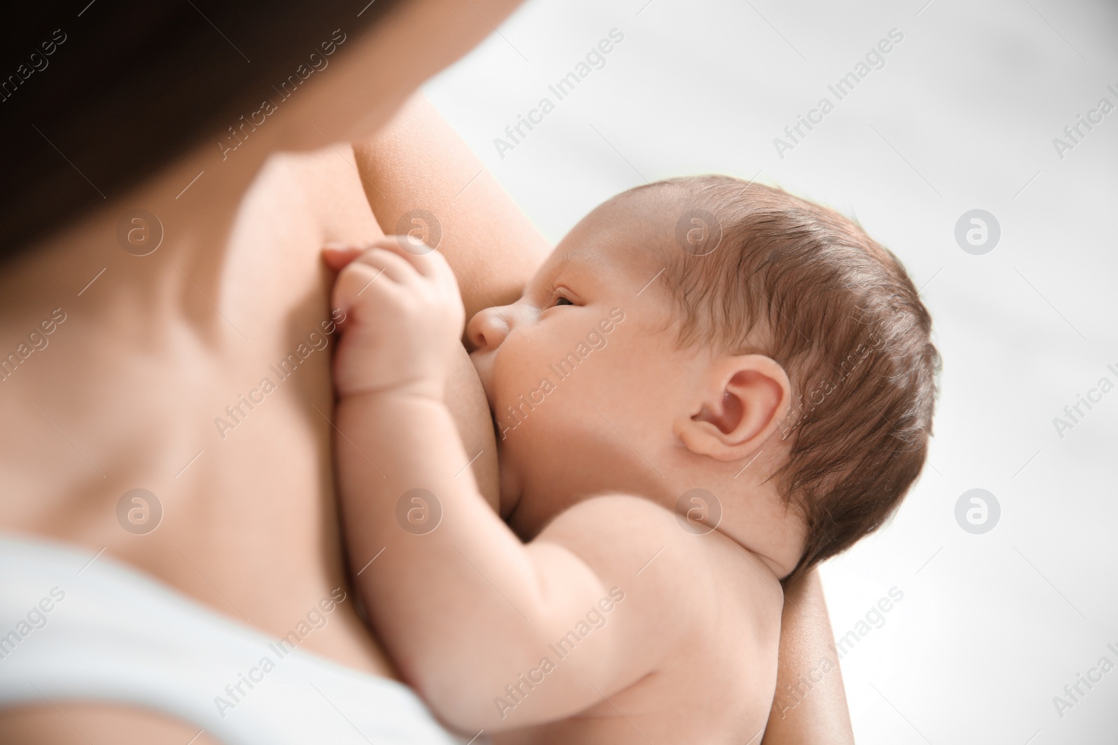 Photo of Young woman breastfeeding her baby on light background, closeup