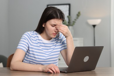 Overwhelmed woman sitting with laptop at table indoors