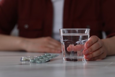 Photo of Woman with glass of water and antidepressant pills at white marble table, closeup