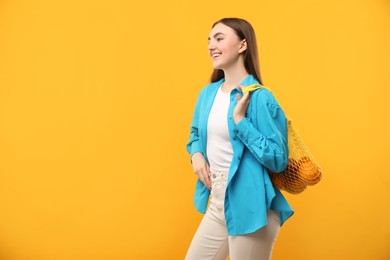 Woman with string bag of fresh oranges on orange background, space for text