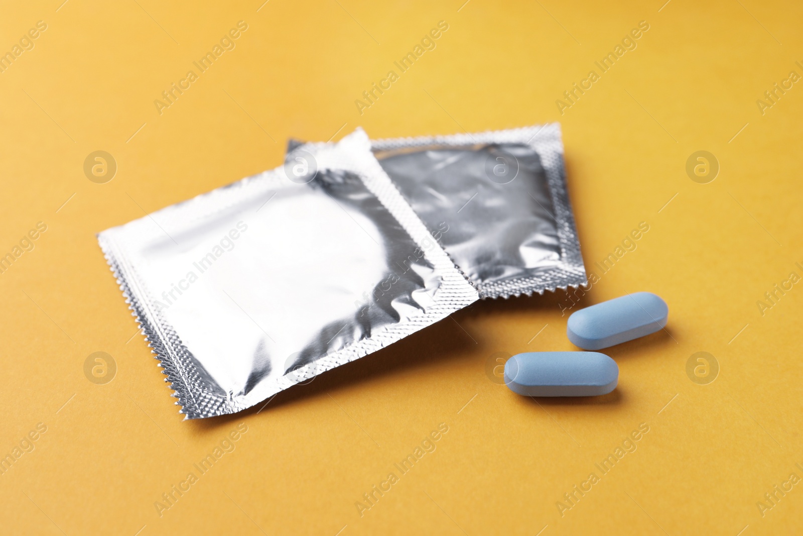 Photo of Pills and condoms on orange background. Potency problem