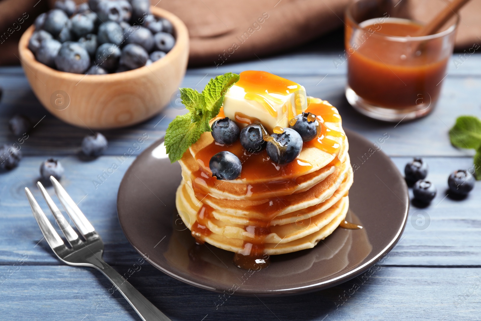 Photo of Delicious pancakes with fresh blueberries, butter and syrup on blue wooden table