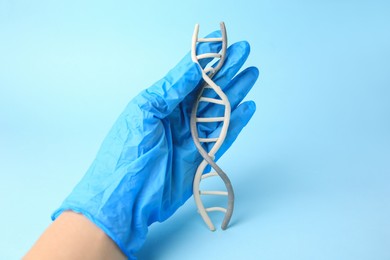 Photo of Scientist holding DNA molecule model made of colorful plasticine on light blue background, closeup