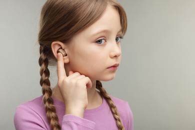 Photo of Little girl with hearing aid on grey background. Space for text