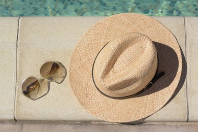 Photo of Stylish hat and sunglasses near outdoor swimming pool on sunny day, flat lay. Beach accessories