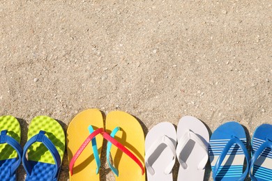 Photo of Many different flip flops on sand, flat lay. Space for text