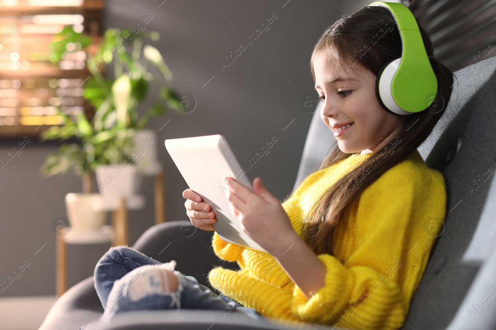 Photo of Cute little girl with headphones and tablet listening to audiobook at home