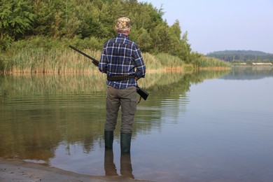 Man with hunting rifle near lake outdoors, back view