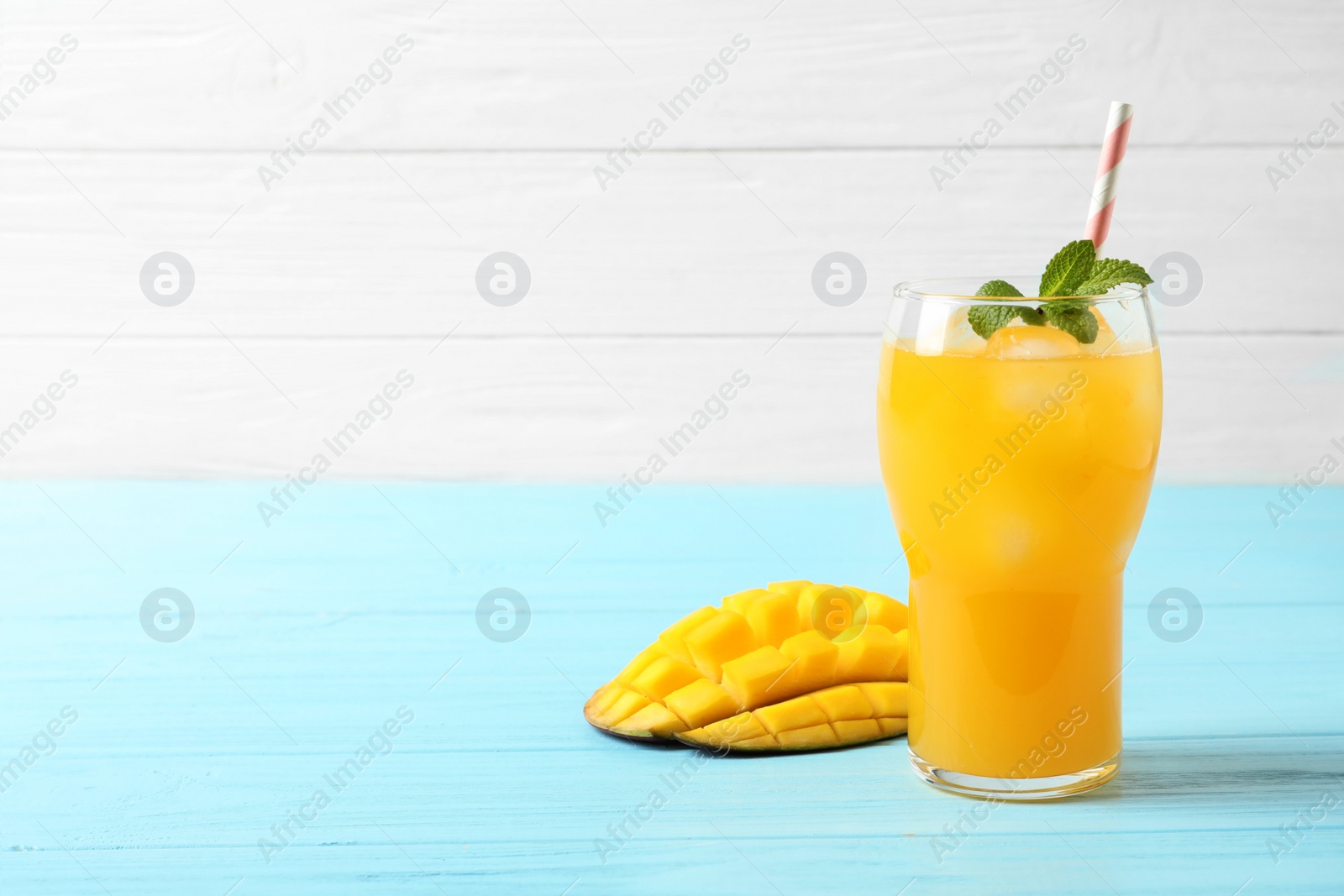 Photo of Fresh mango drink and cut fruit on blue wooden table. Space for text