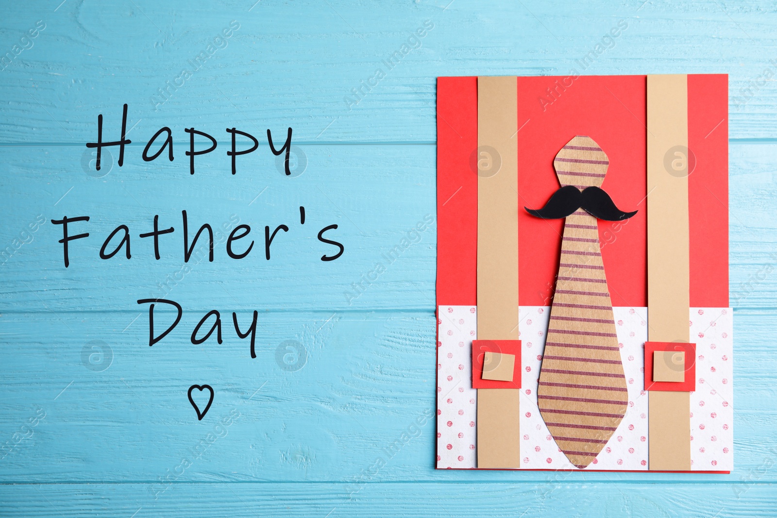 Image of Handmade card and phrase HAPPY FATHER'S DAY on light blue wooden table, top view