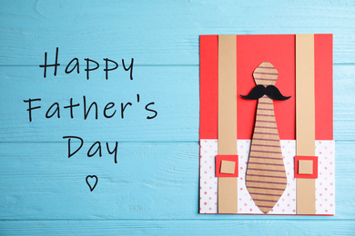 Image of Handmade card and phrase HAPPY FATHER'S DAY on light blue wooden table, top view