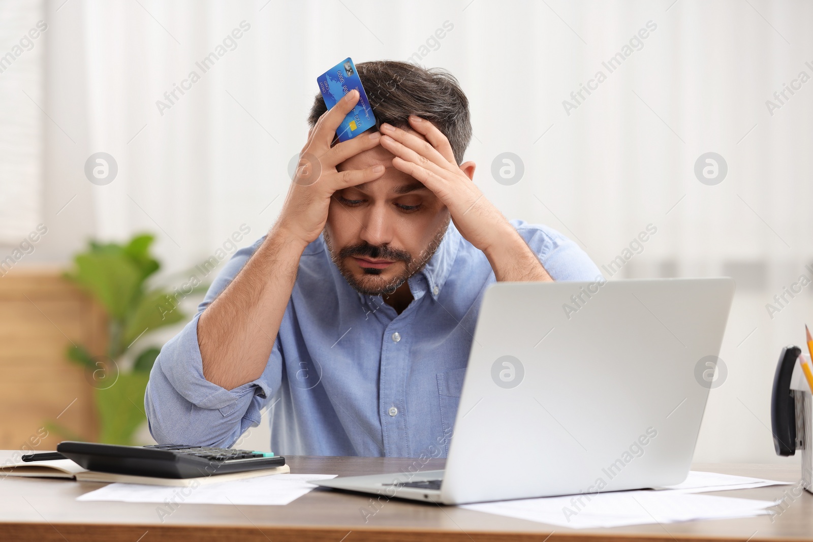 Photo of Confused man with debt notification and credit card planning budget at table in room. Financial problem