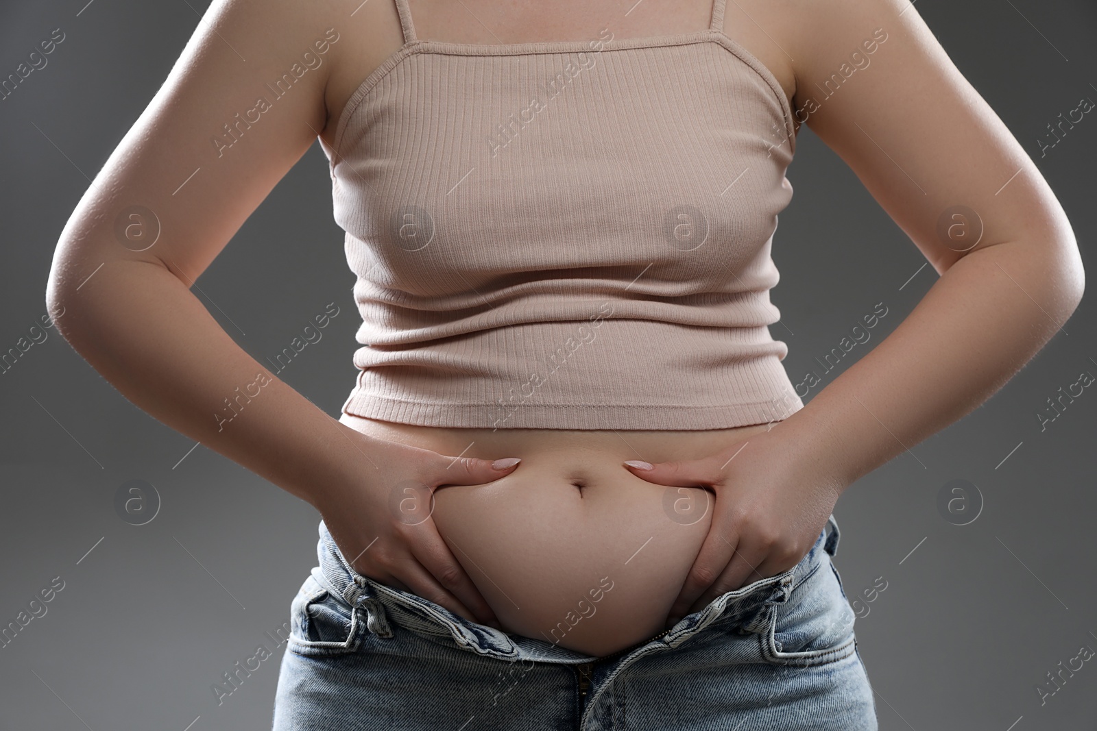 Photo of Woman touching belly fat on grey background, closeup. Overweight problem
