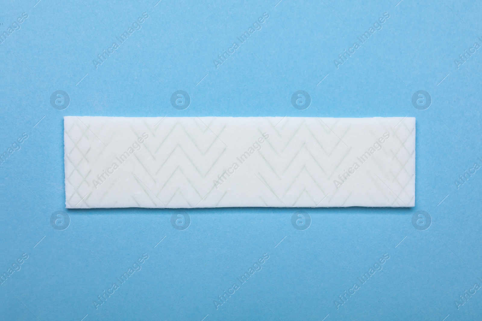 Photo of Stick of tasty chewing gum on light blue background, top view