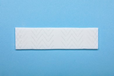 Photo of Stick of tasty chewing gum on light blue background, top view