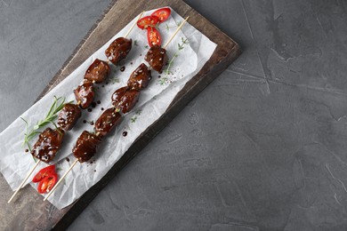 Photo of Skewers with pieces of tasty chicken meat glazed in soy sauce, herbs and cut chili pepper on grey textured table, top view. Space for text