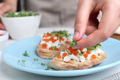 Photo of Woman putting microgreens onto sandwich with caviar at table, closeup