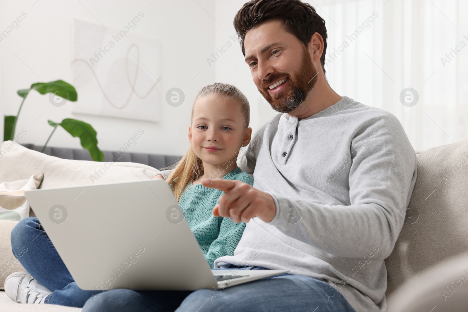 Photo of Happy man and his daughter with laptop on sofa at home