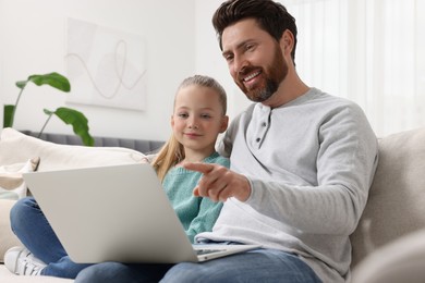Happy man and his daughter with laptop on sofa at home
