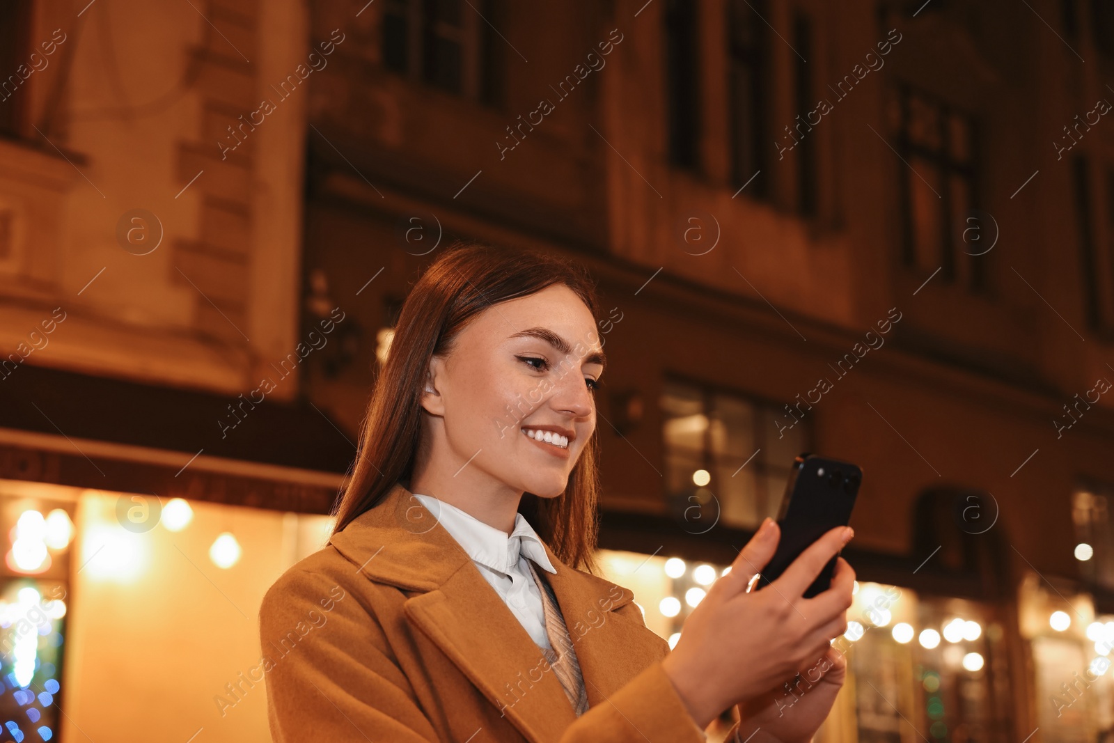 Photo of Smiling woman using smartphone on night city street