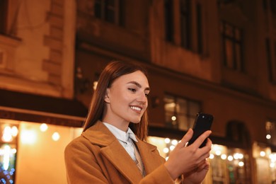 Smiling woman using smartphone on night city street