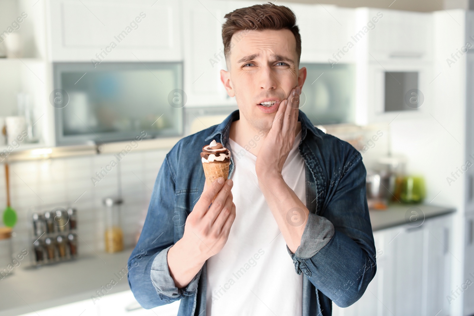 Photo of Young man with sensitive teeth and cold ice cream in kitchen