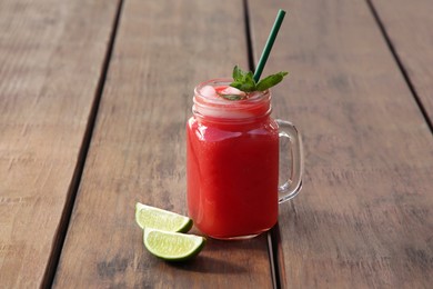 Photo of Delicious watermelon drink in mason jar and fresh lime on wooden table