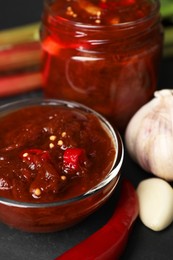 Tasty rhubarb sauce and ingredients on black table, closeup