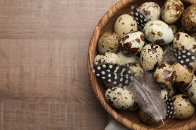 Photo of Speckled quail eggs and feathers on wooden table, top view. Space for text